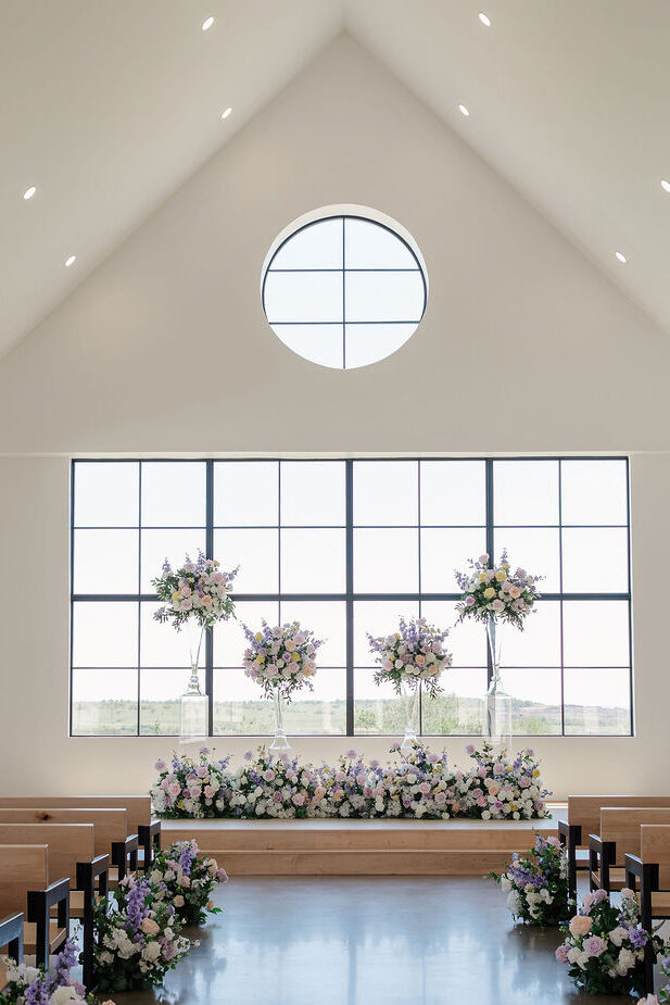 A decorated ceremony set up in front of big glass windows at the Grace Manor Wedding Venue 